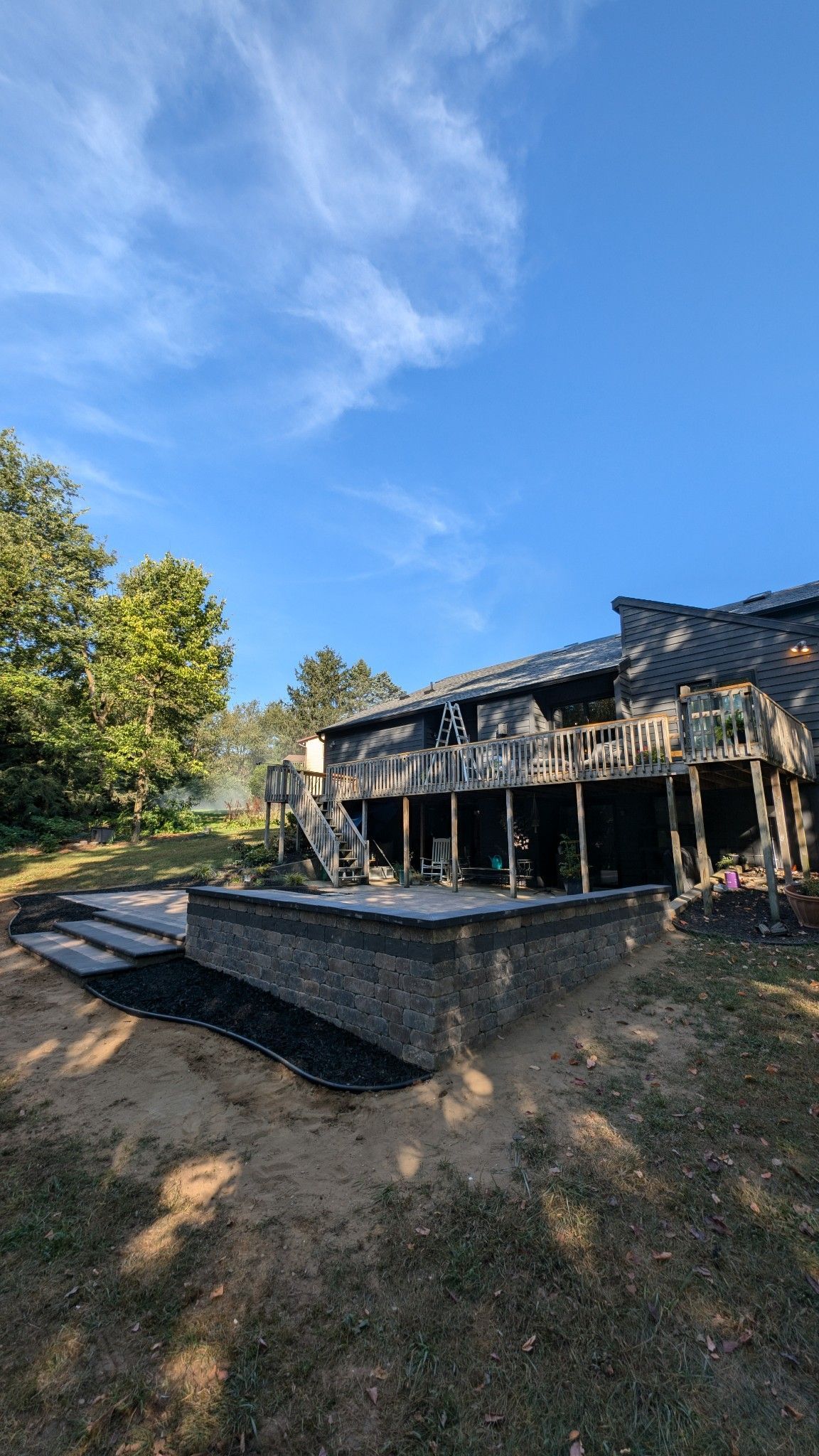 A large house with a large deck is sitting in the middle of a field.