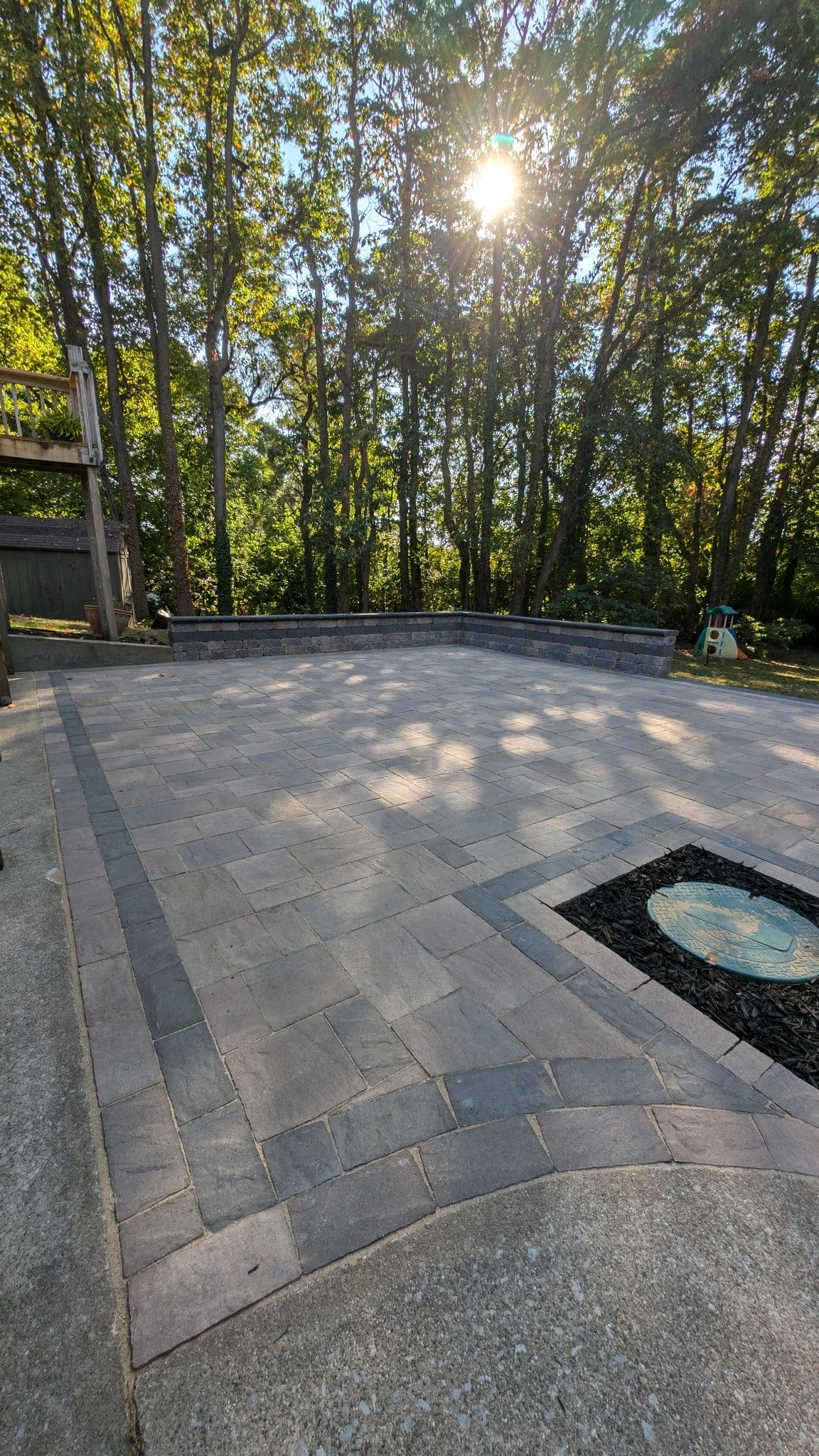 A patio with trees in the background and the sun shining through the trees.