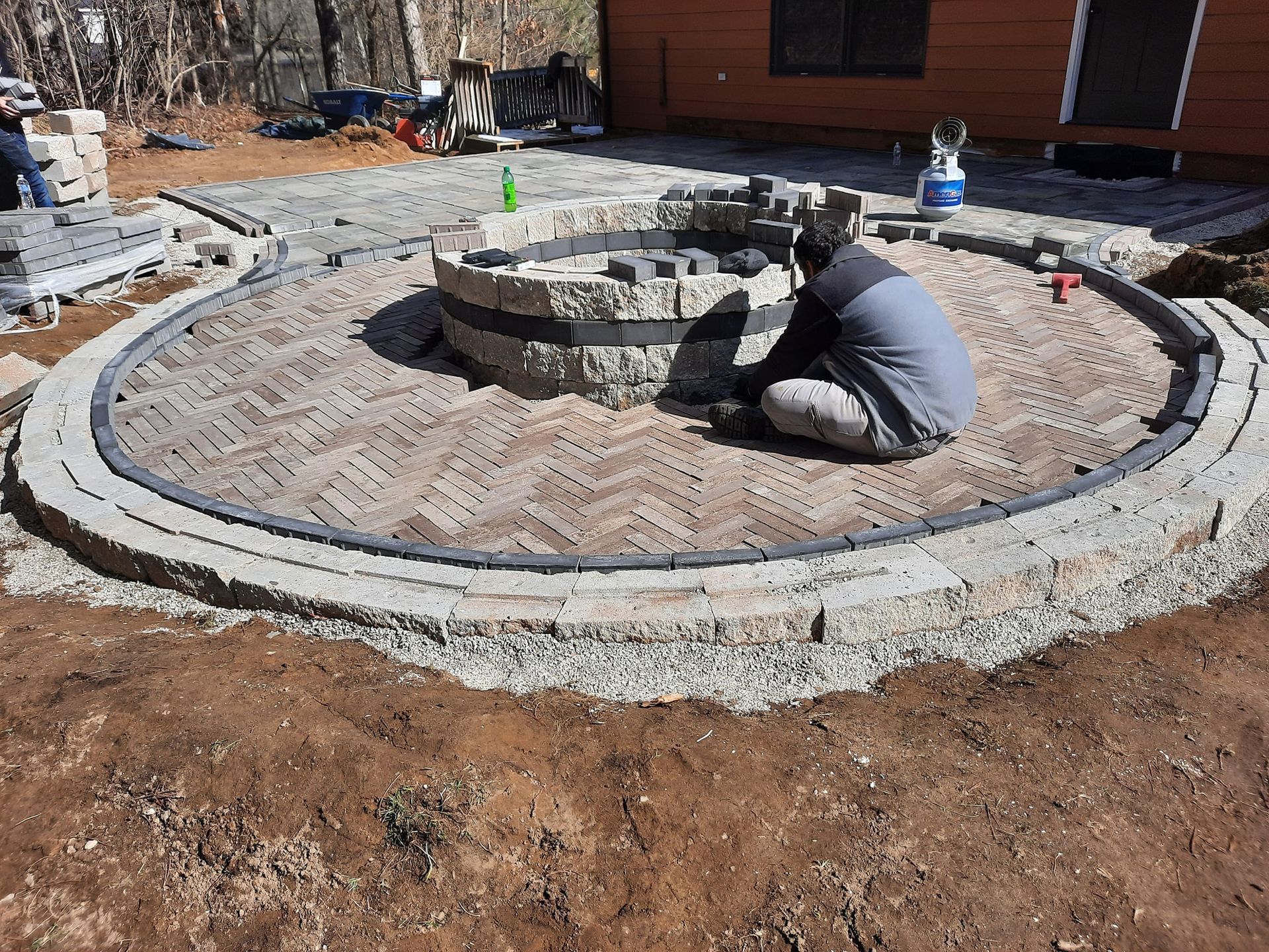 A man is kneeling in the dirt next to a fire pit.
