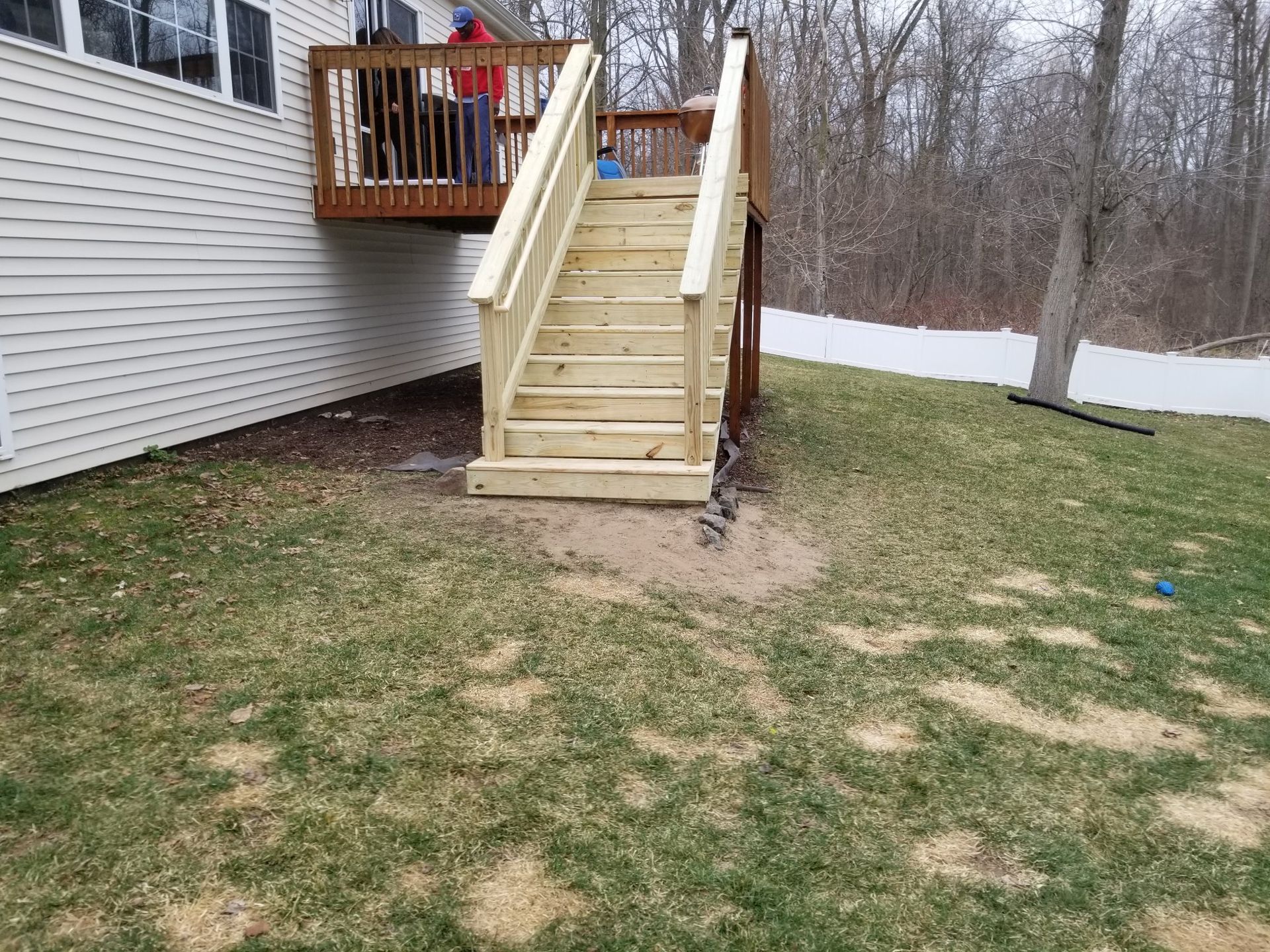 A wooden deck with stairs leading up to it is in the backyard of a house.