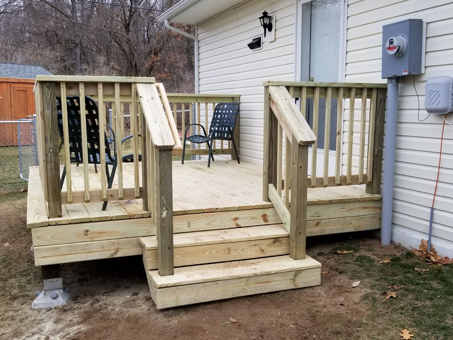 A wooden deck with chairs and stairs is in front of a house.