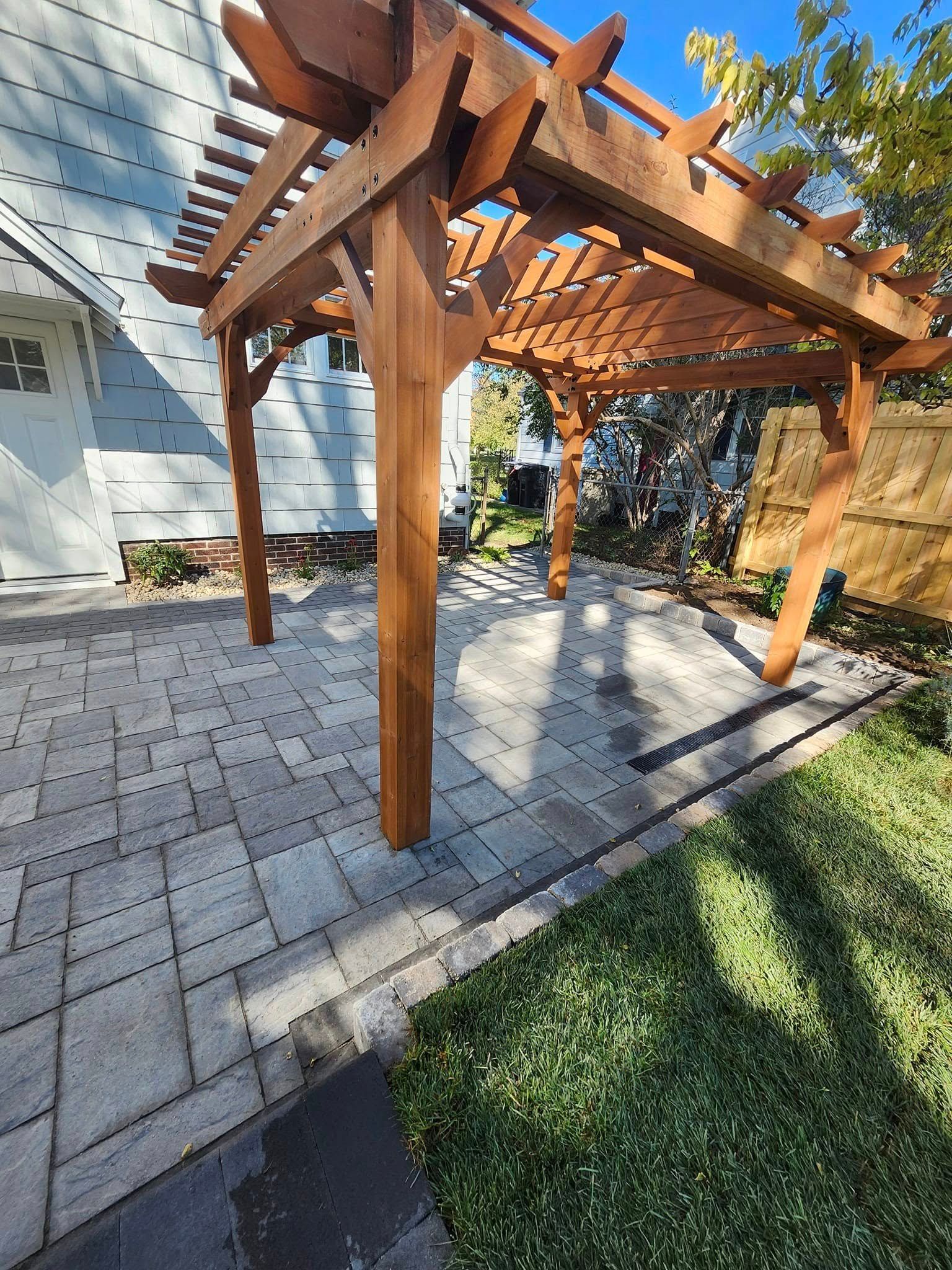 A wooden pergola is sitting on top of a patio next to a house.