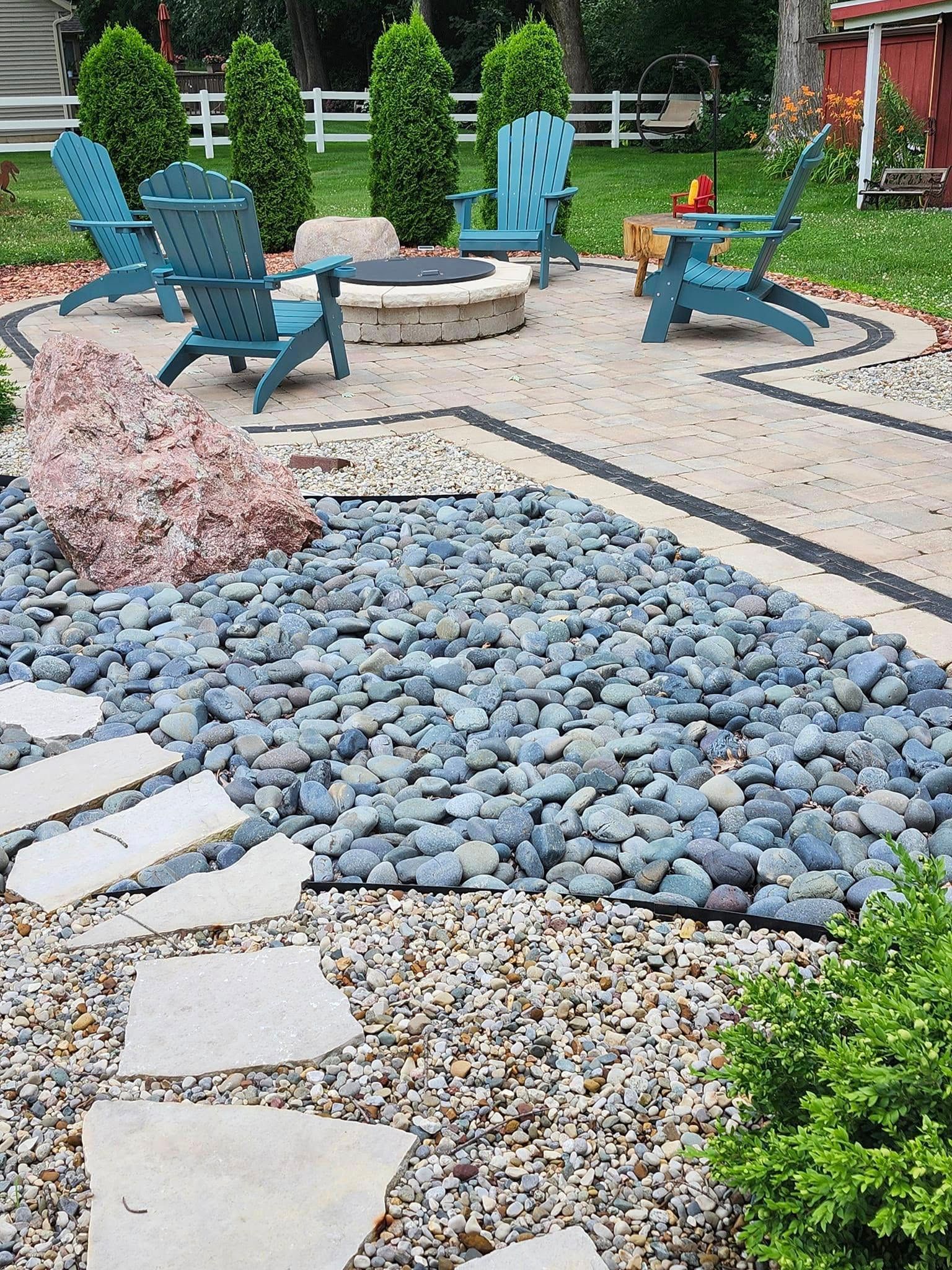 A patio with blue chairs and a fire pit surrounded by rocks.