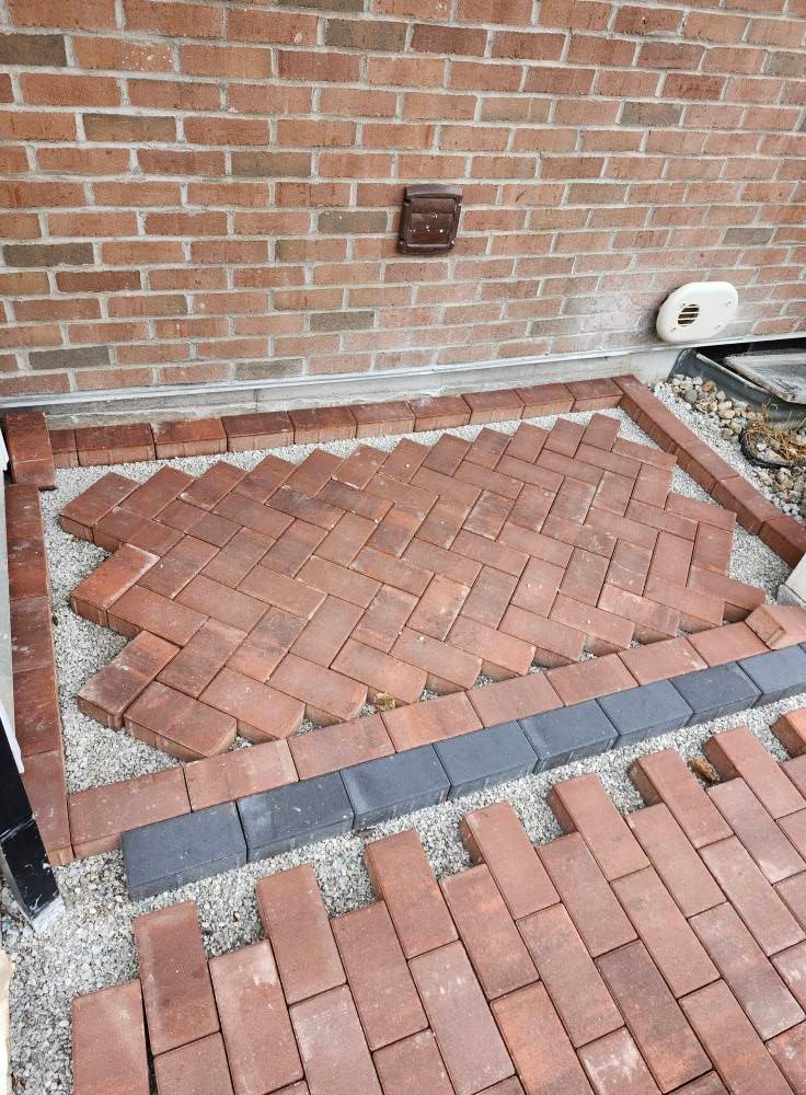 A brick walkway is being built in front of a brick wall.