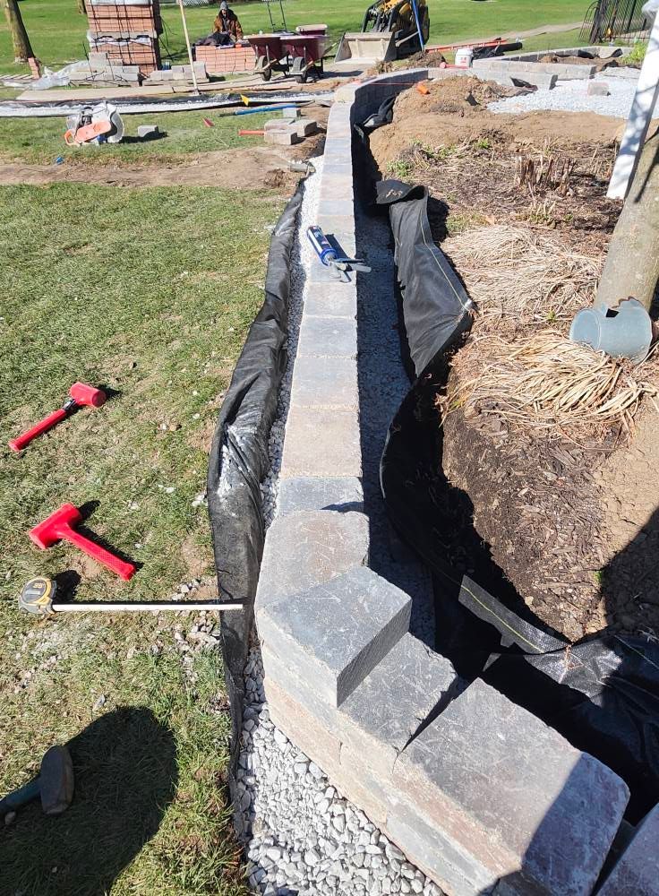 A brick wall is being built in a yard with a hose coming out of it.
