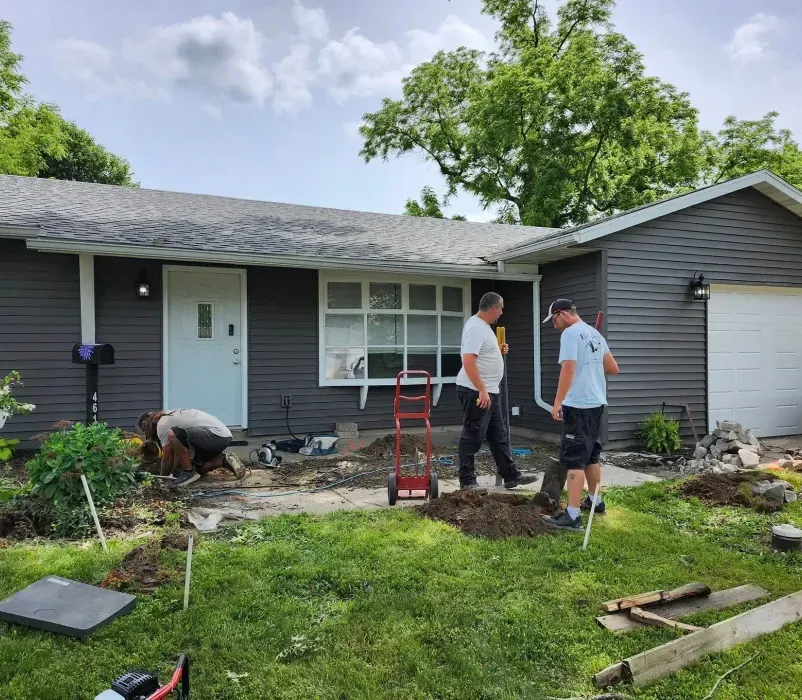 Two men are digging in front of a house.