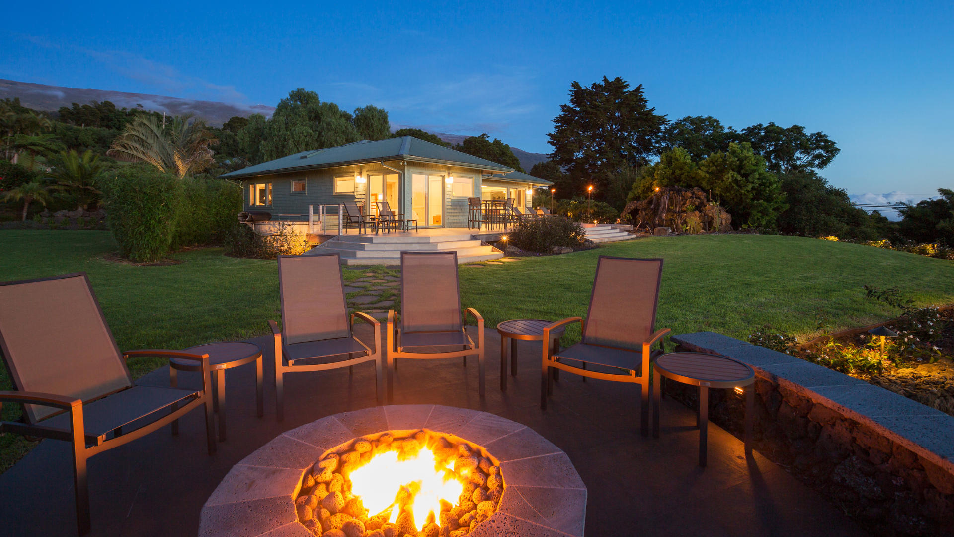 A fire pit with chairs around it in front of a house.