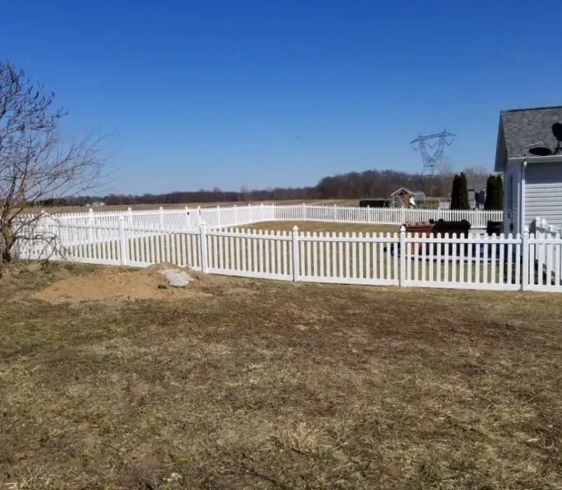 A white picket fence surrounds a yard in front of a house.