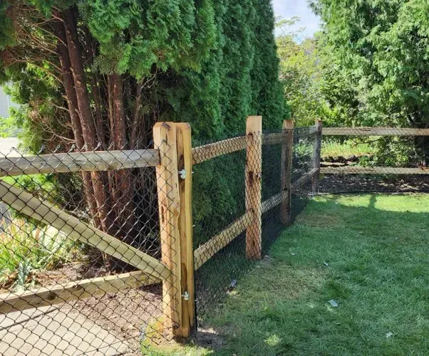 A wooden fence with a chain link fence surrounding a lush green yard.