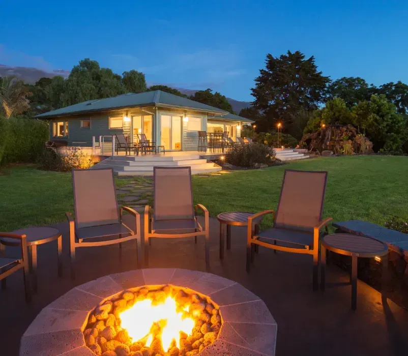 A fire pit with chairs around it in front of a house.