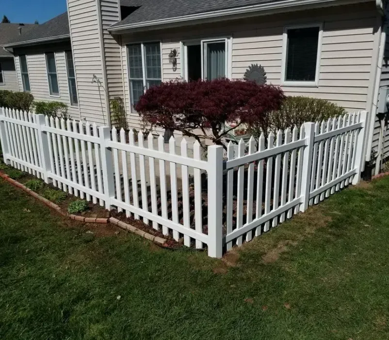 A white picket fence is in front of a house.