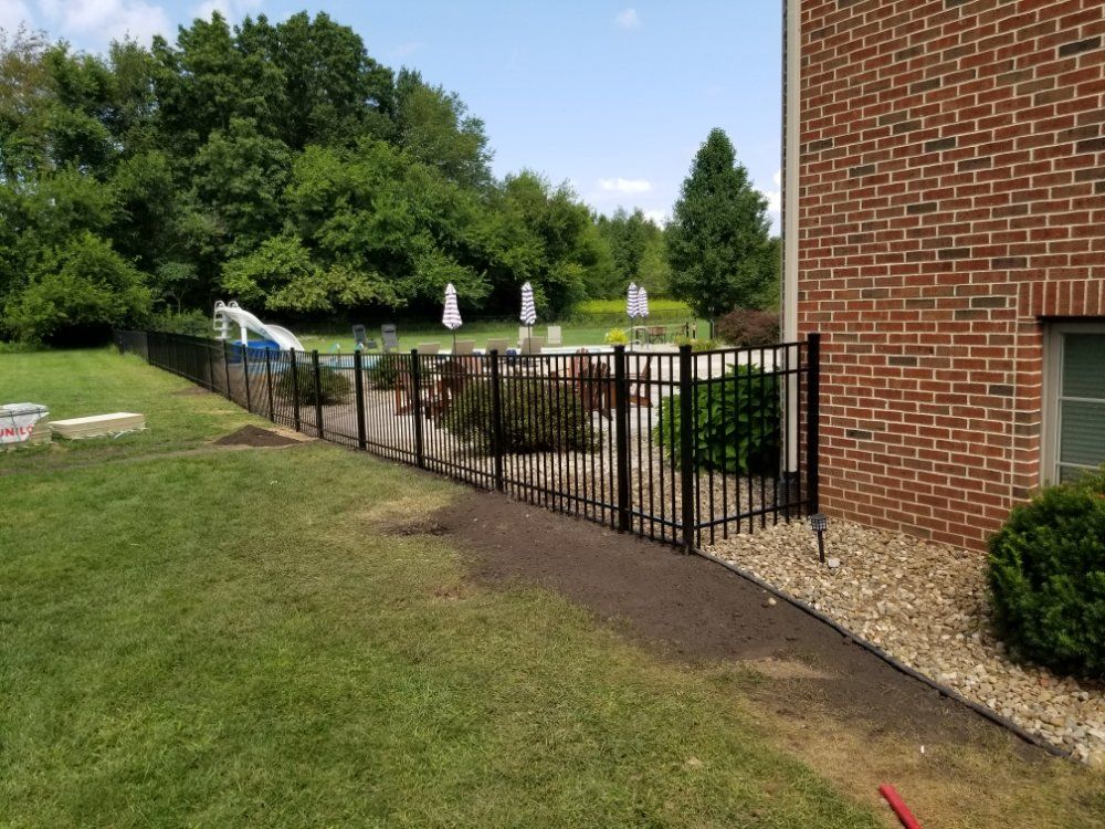 A black fence surrounds a brick house with a pool in the background.
