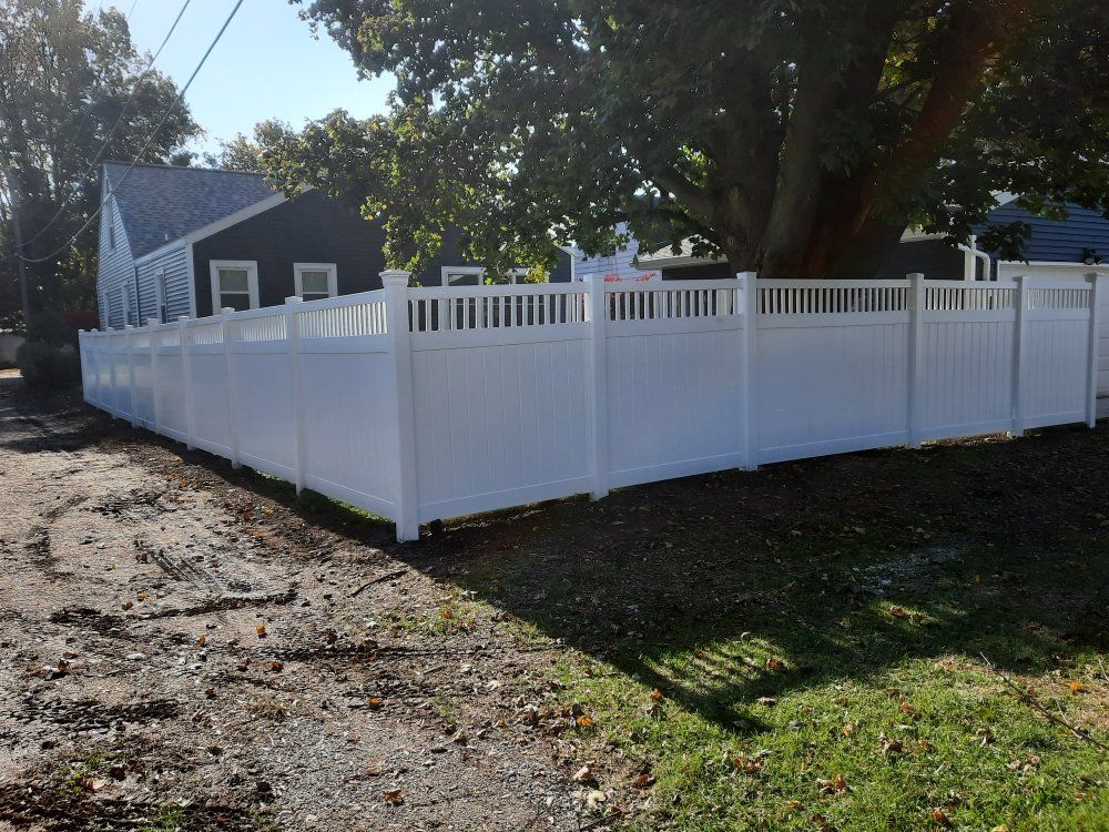 A white fence is surrounding a yard in front of a house.