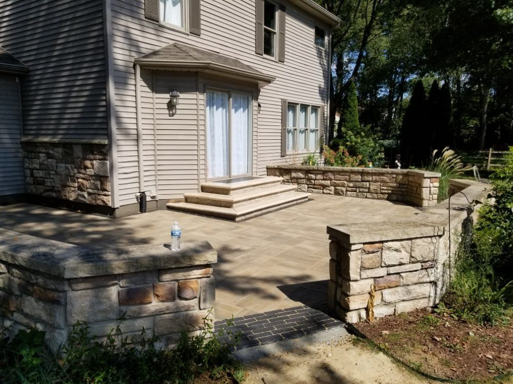 A house with a stone wall and a patio in front of it.