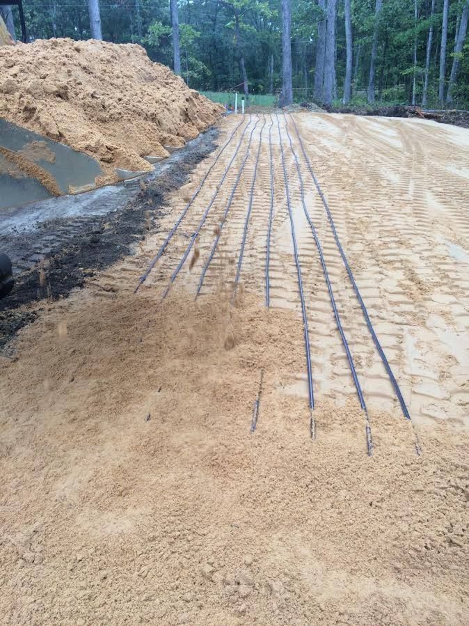 Gravel road under construction with exposed rebar and piles of dirt in a wooded area