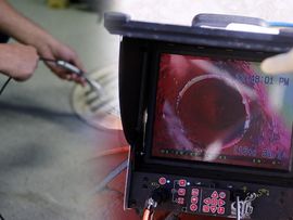Handheld inspection monitor showing a red-lit pipe interior while a person holds a probe nearby