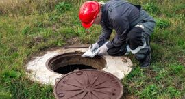 Worker in red hard hat cleaning an open manhole on grass
