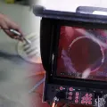 Inspection monitor showing a red pipe interior with a circular opening and control panel below