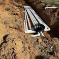 White PVC pipes laid in a dirt trench, with a black circular pipe fitting at one end.