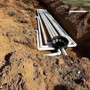White PVC pipes laid in a dirt trench, with a black circular pipe fitting at one end.