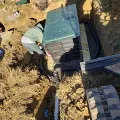 Worker beside a buried black utility box with a green lid in a dirt trench