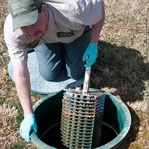 Worker in gloves inspecting a coiled pipe inside a green underground utility access hole.