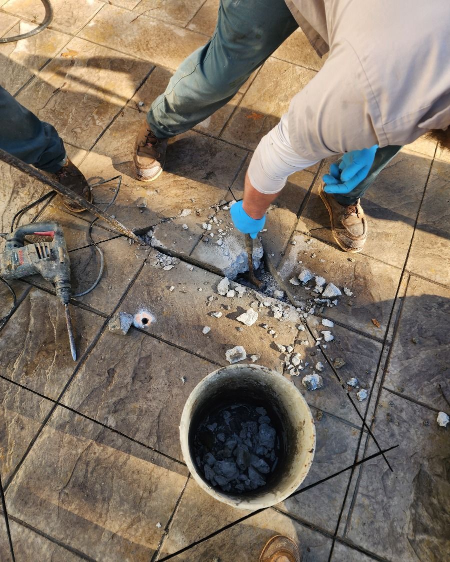 Workers removing broken concrete around a circular hole on a stone pavement, using blue gloves and tools