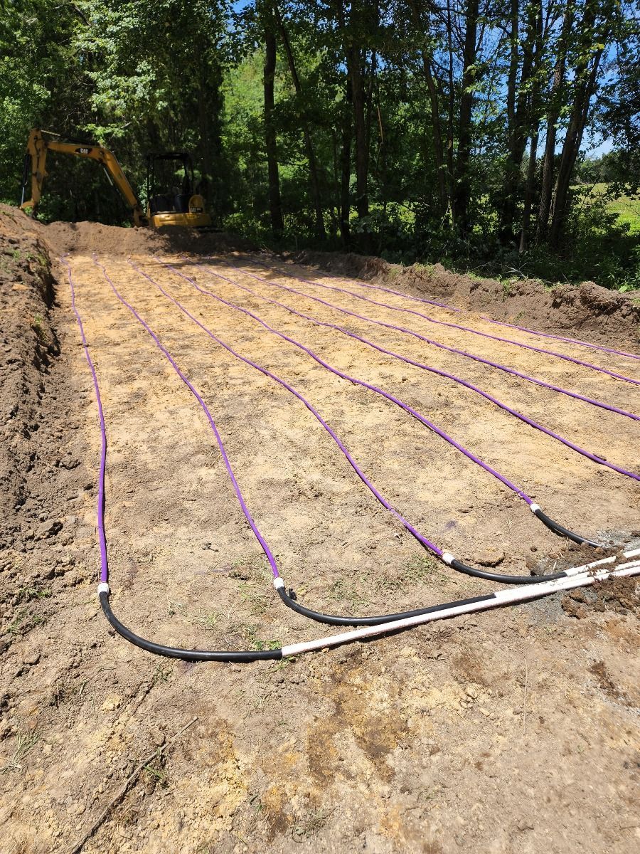 Freshly cleared dirt lot with purple irrigation lines laid across it beside a wooded edge