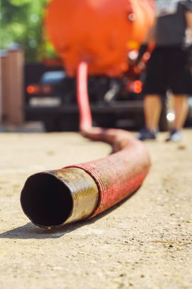 Red fire hose nozzle lying on pavement, with blurred firefighters and a fire truck in the background