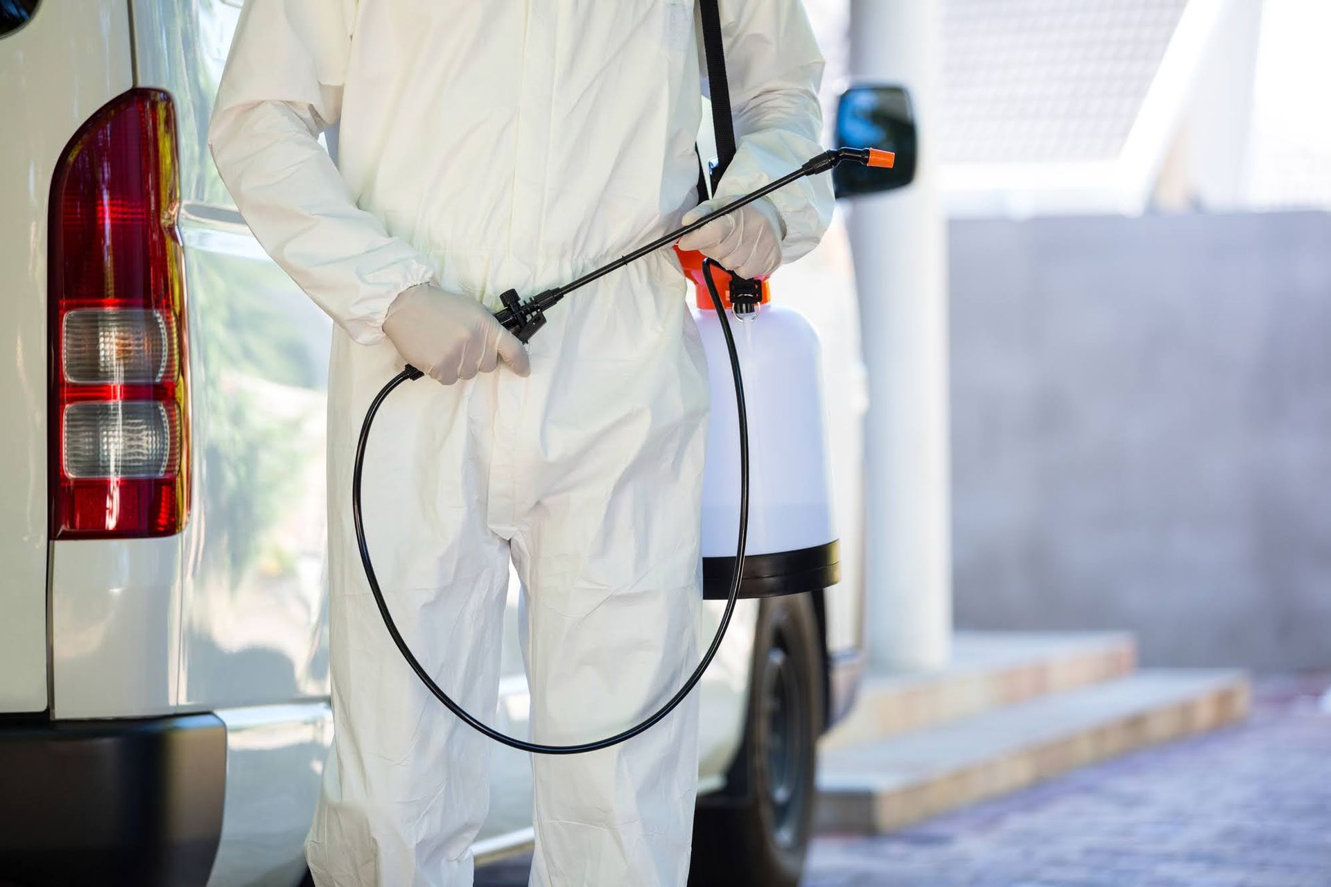 A man in a protective suit is spraying pests with a sprayer.