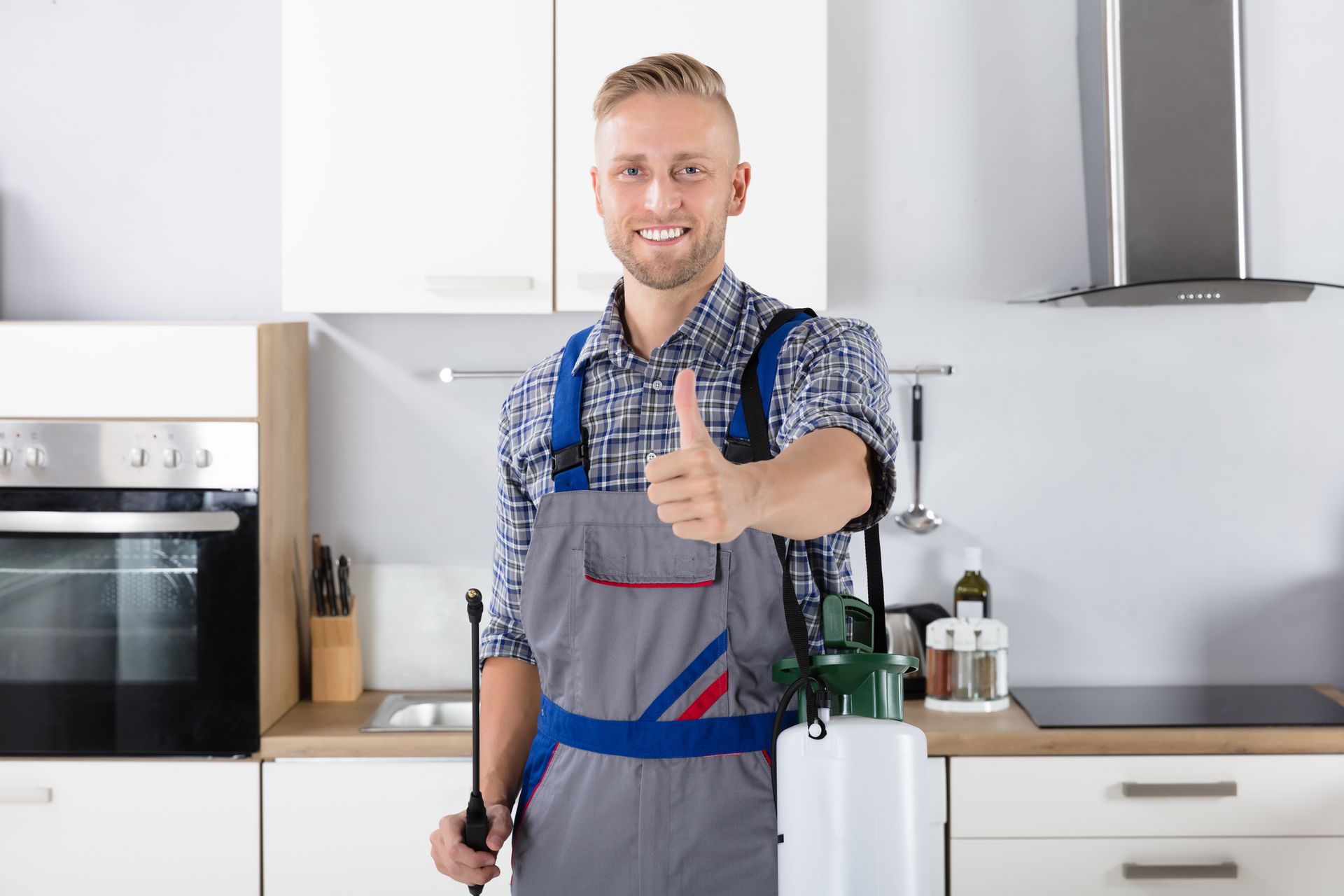 Smiling pest control worker with pesticide container in kitchen providing pest control services.