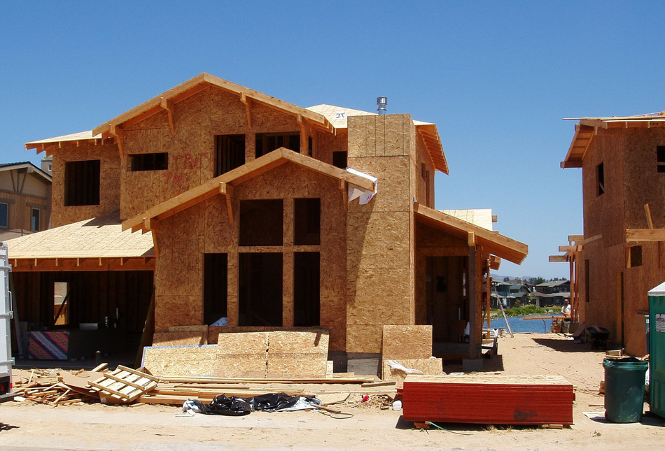 A two-story house under construction with wood framing, against a clear blue sky.