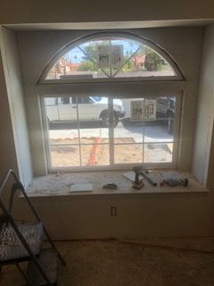 Window with a rounded top, showing a view of a street. A ladder sits nearby.