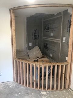 Framed curved wall opening. Interior construction, with wooden supports, grey waterproof panels, and exposed framing.