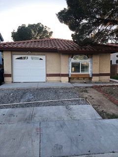 Tan house with a white garage door, red-tiled roof, and an arched window. Gravel yard and concrete driveway.