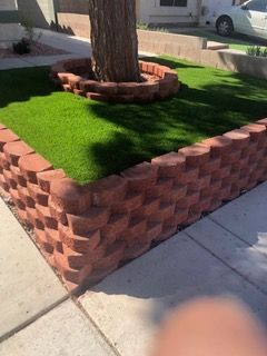 Red brick retaining wall surrounds artificial turf and tree in a residential yard.