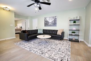 Living room with black leather sectional, rug, and bookshelf against a light green wall.