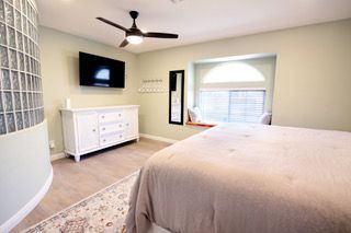 Bedroom with a bed, dresser, TV, and a window seat. Light green walls, beige bedding, and a glass block wall.