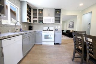 Gray kitchen with white appliances, wooden floor, and a dining table.