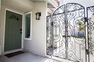 Green front door, ornate black gate, neutral-colored house exterior.