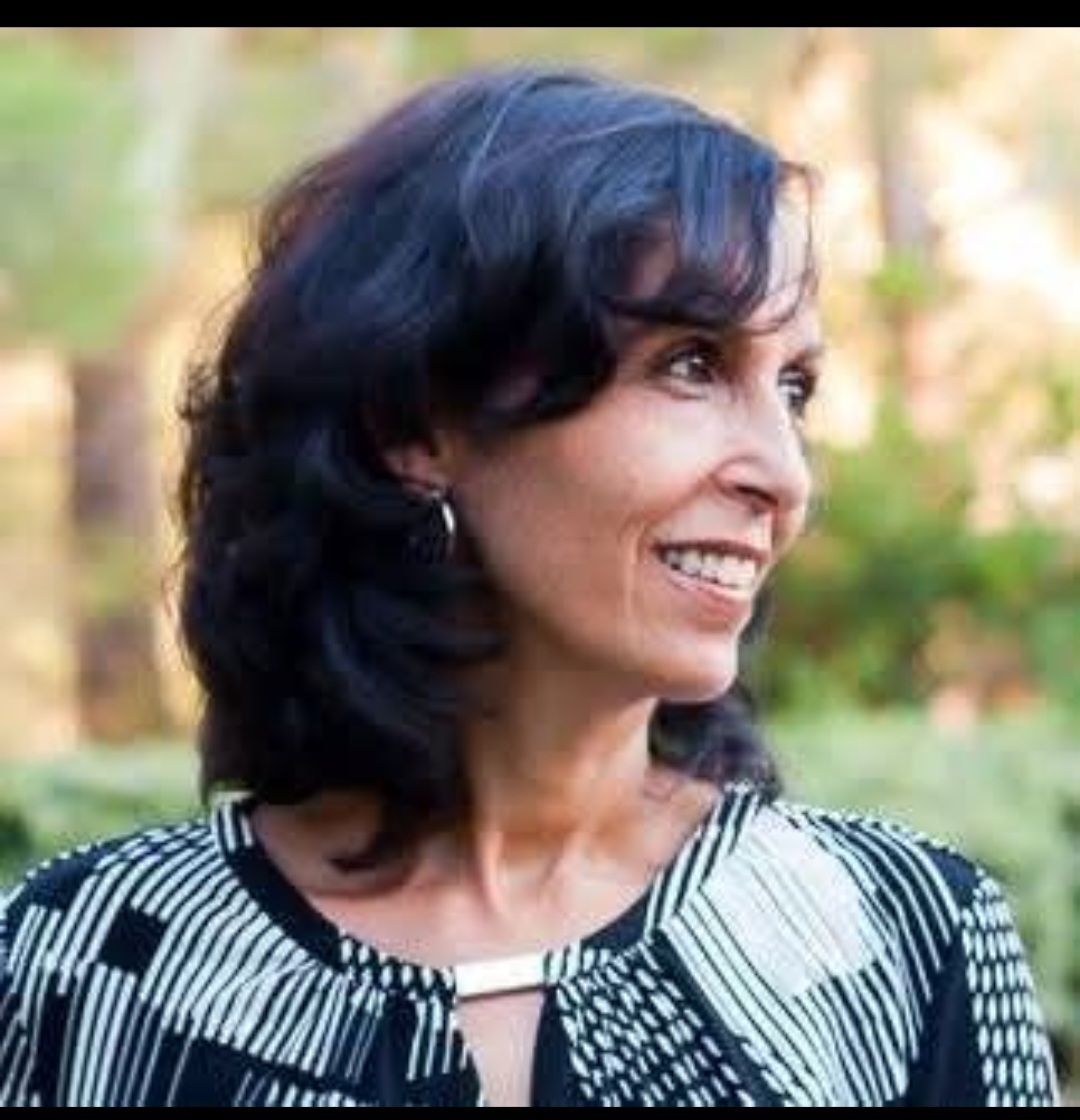 Woman with dark hair and a patterned blouse smiles outdoors.