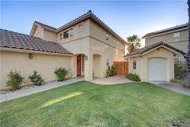 Two-story beige house with brown tile roof, green lawn, small garage, and wooden gate.