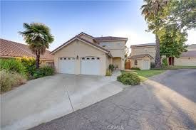 Two-story beige house with a driveway, garage, and small yard; Palm trees and blue sky.