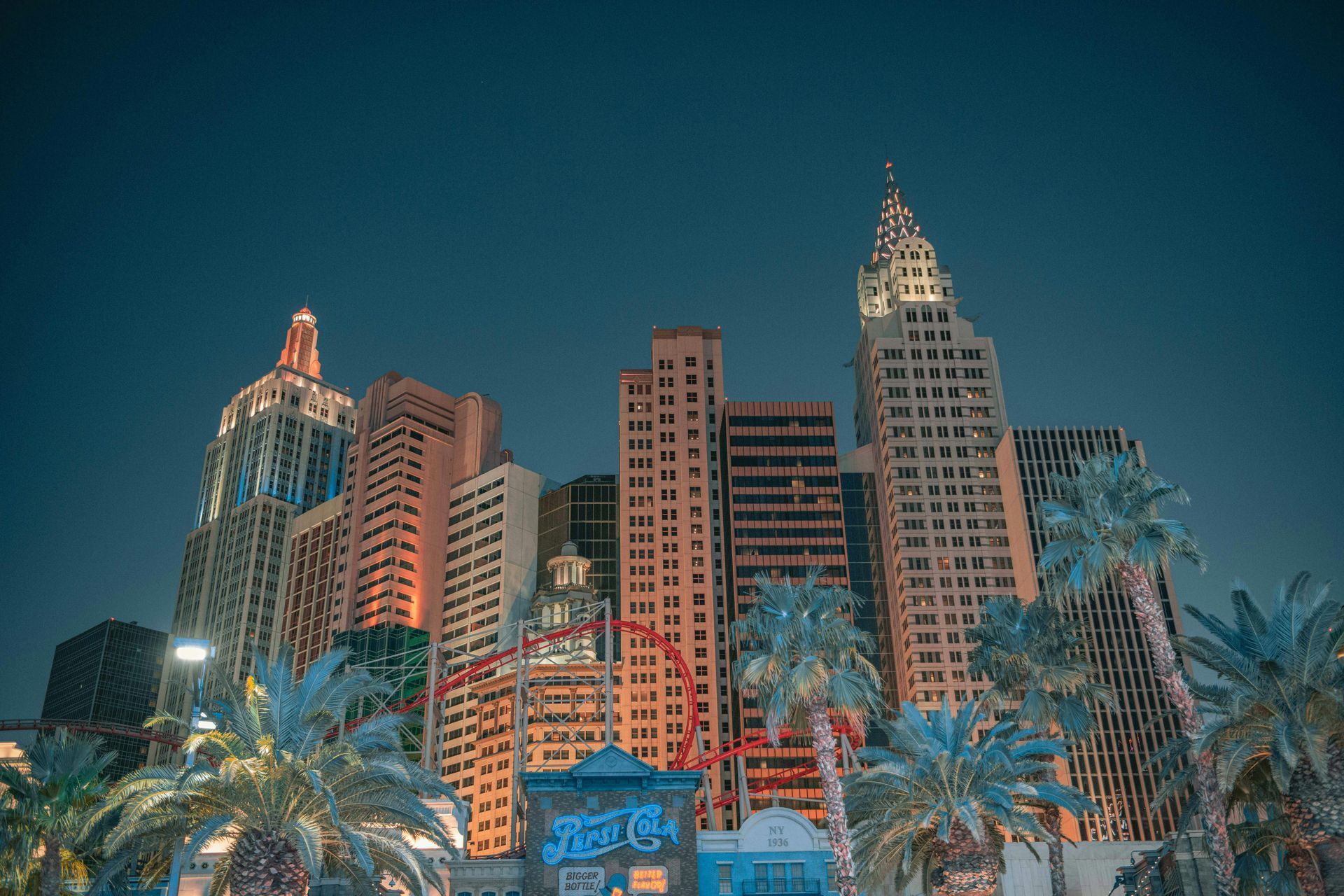 New York-themed cityscape at night, featuring various skyscrapers and palm trees, under a dark blue sky.