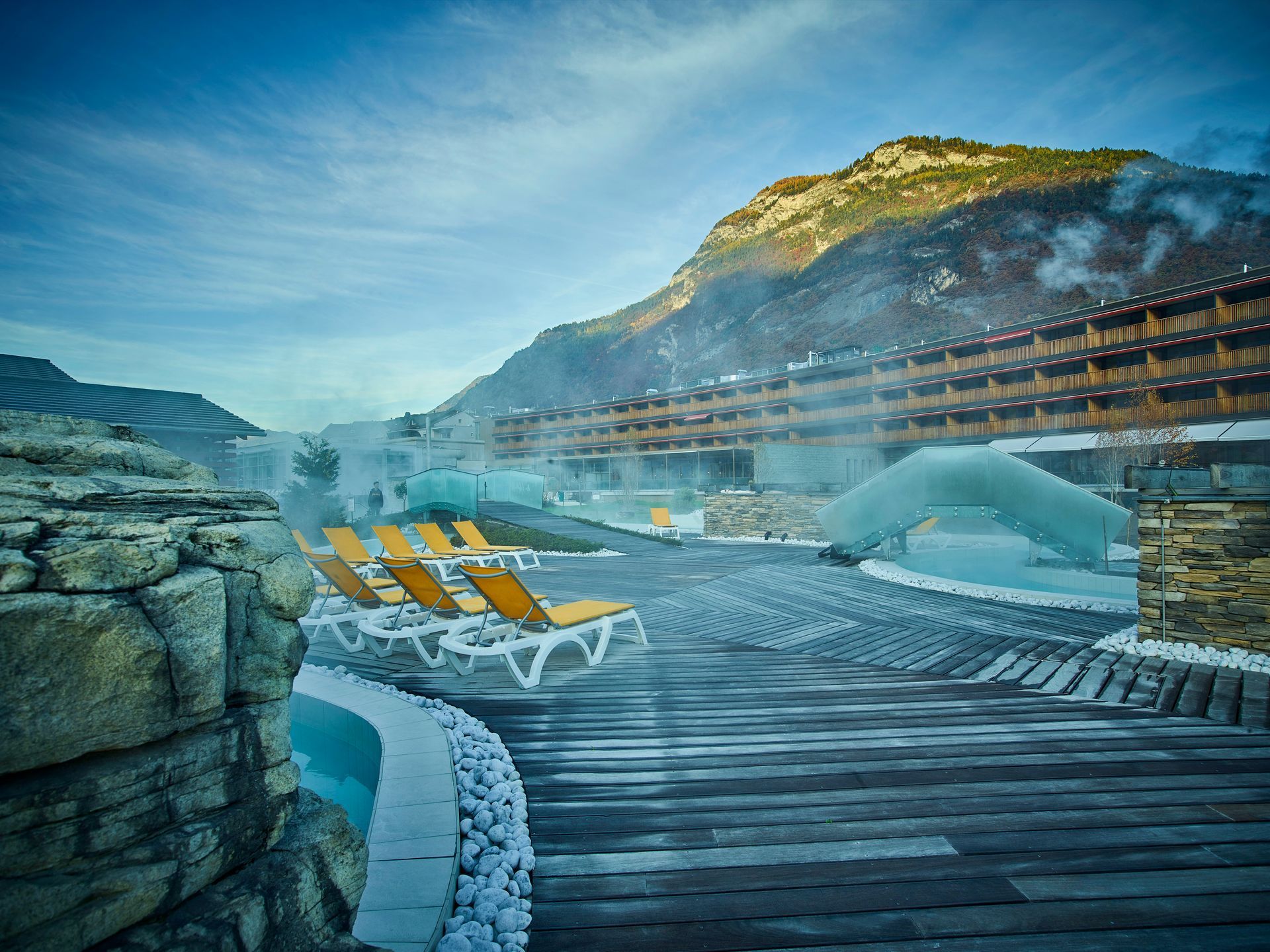 Outdoor spa with lounge chairs, pools, and mountain view.