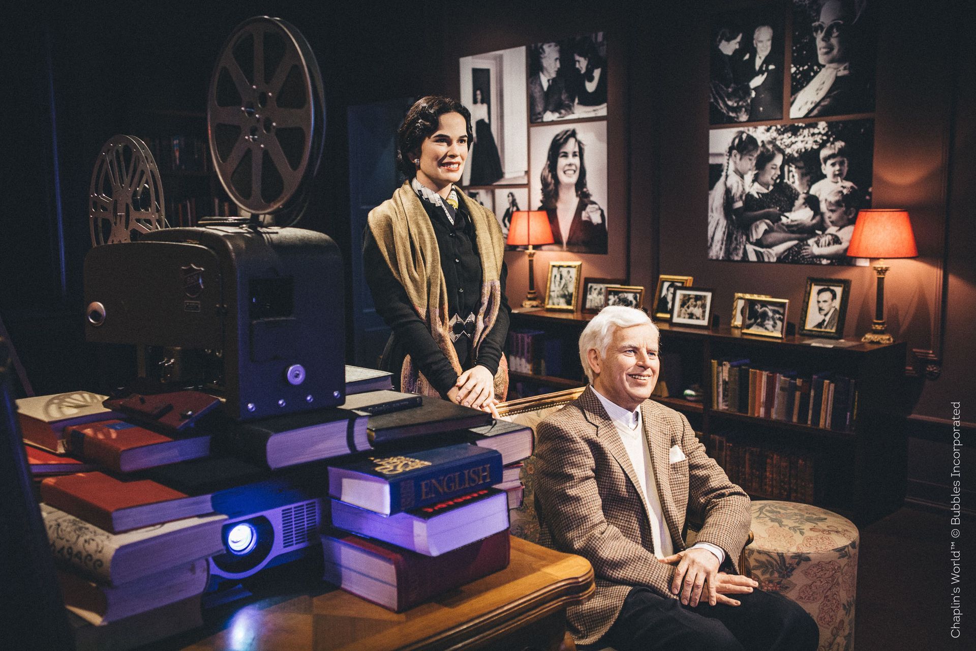 Wax figures of a man and woman in a movie room, with a projector and books.