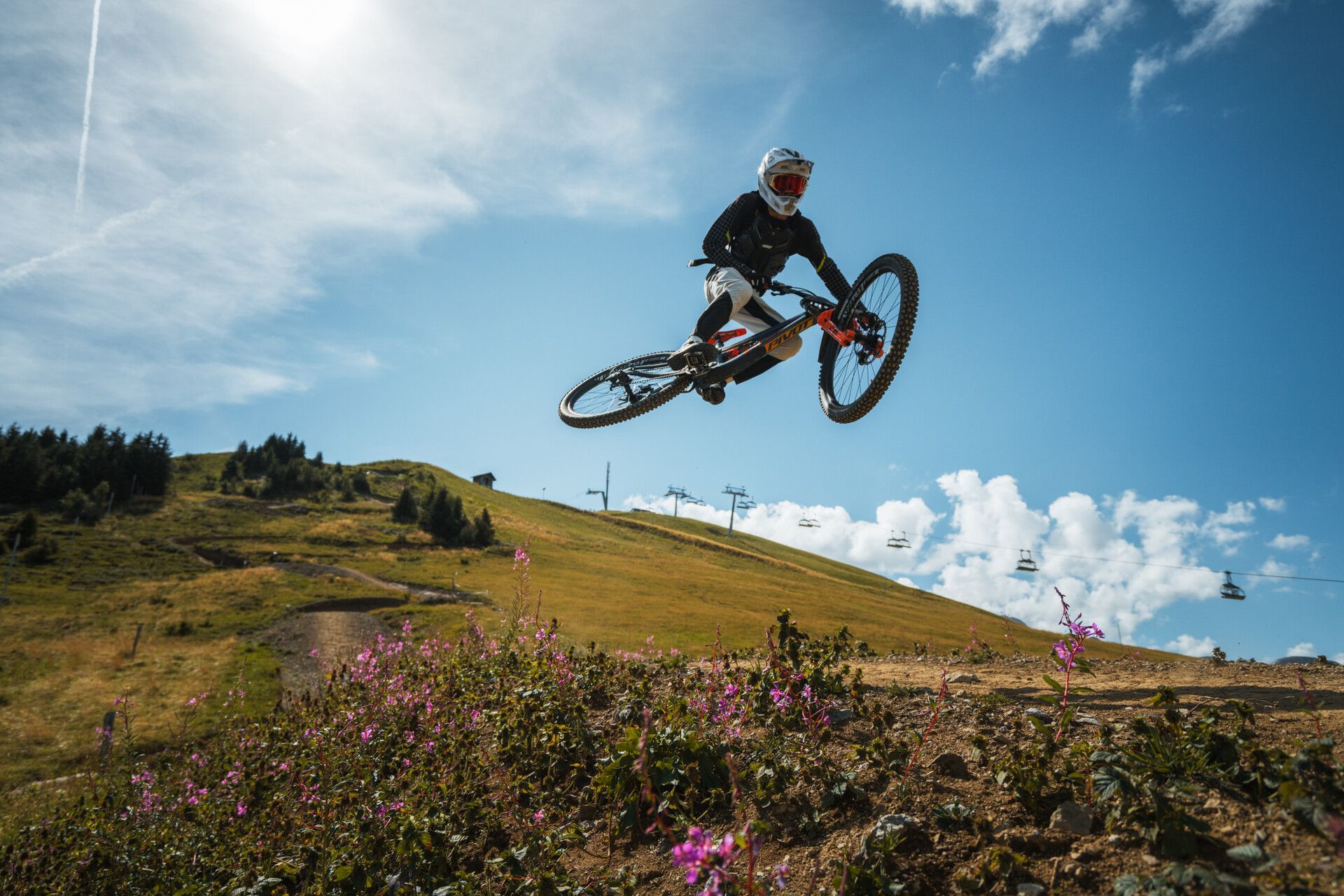 Mountain biker airborne over a grassy hillside under a blue sky with clouds