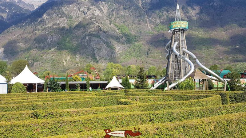 A maze, playground tower, and tents in front of a mountain.