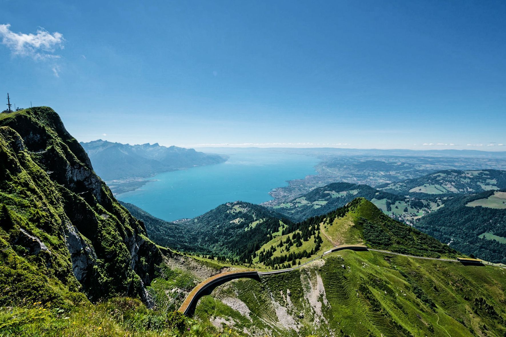 Mountain trail above a green valley and blue bay under a clear sky