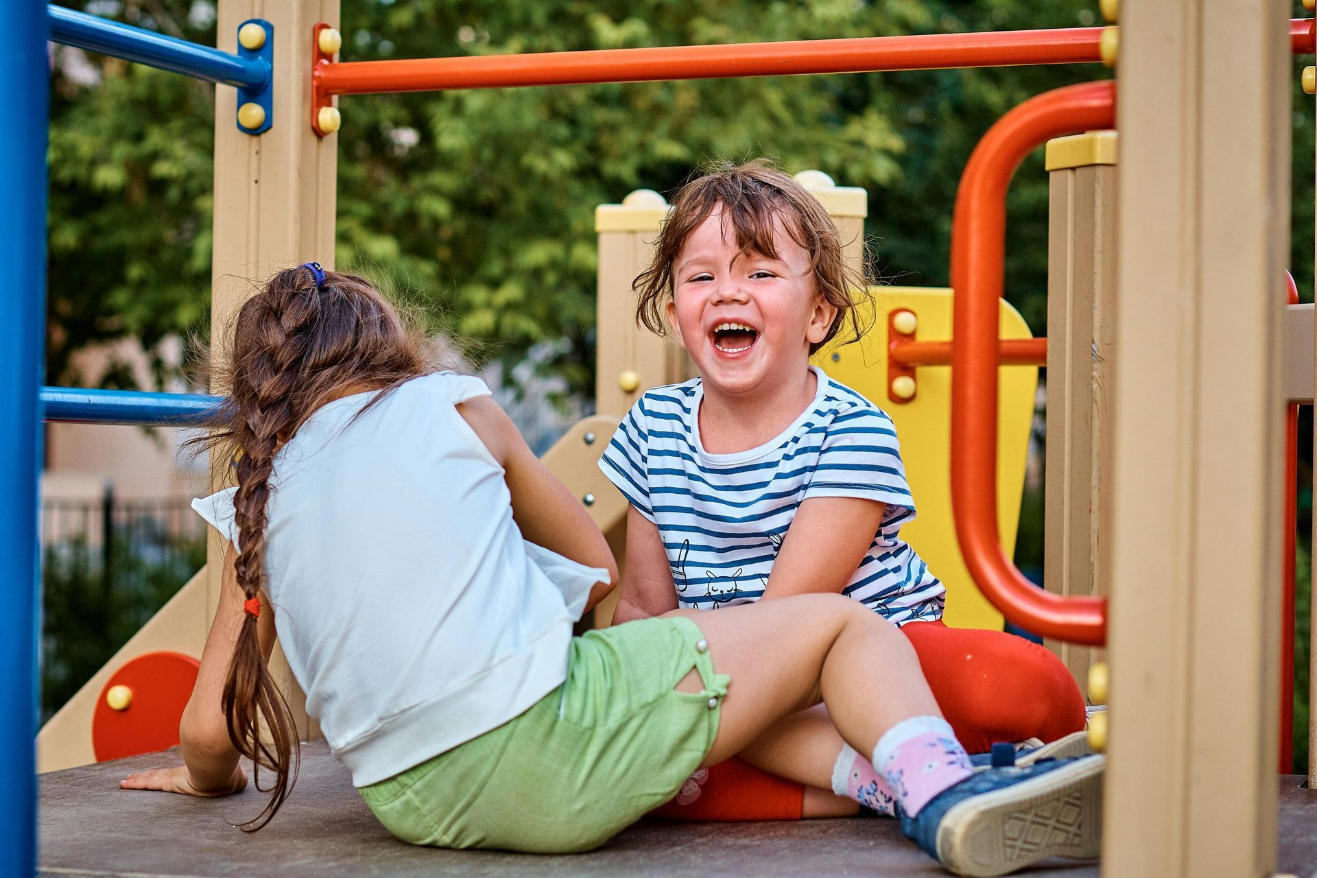Ein Kind rutscht mit Hilfe einer anderen Person eine rote Rutsche hinunter; beide sind in Winterkleidung auf einem verschneiten Spielplatz.